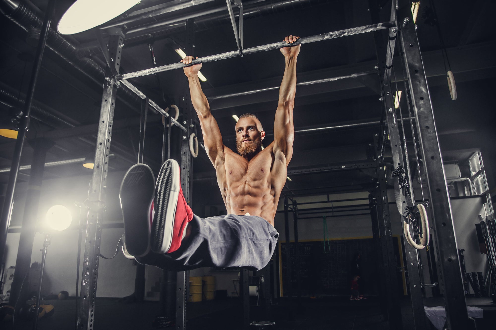 Muscular man performing a hanging exercise on gym rings.