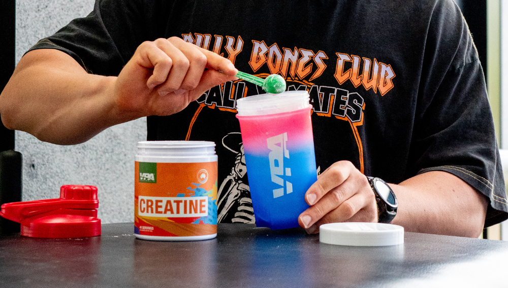 Person mixing a colorful drink with creatine powder on a table.