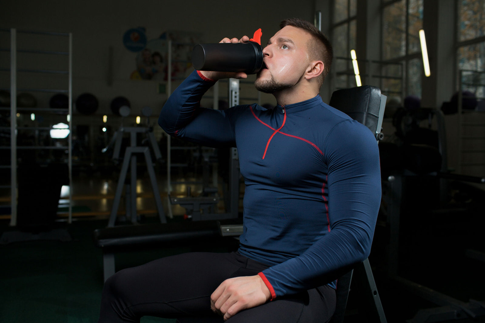 Man in athletic wear drinking from a shaker bottle in a gym.