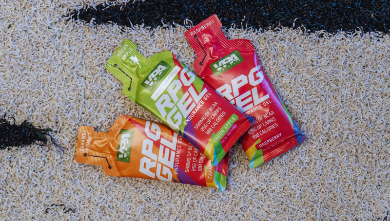 Three sport energy gel packets on a sandy surface.