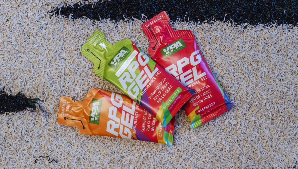 Three sport energy gel packets on a sandy surface.