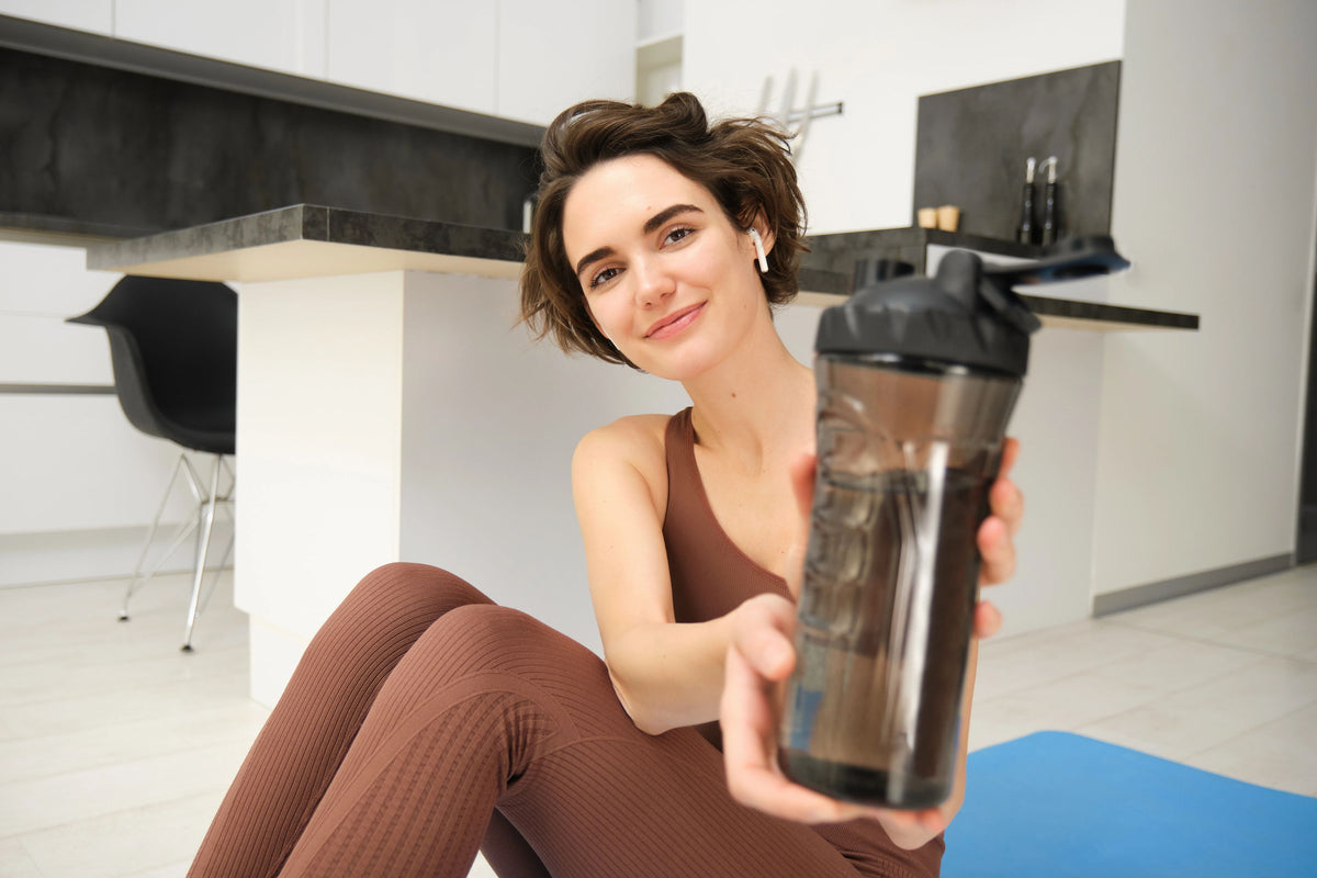 Young woman in athletic wear holding a shaker bottle in a modern kitchen.
