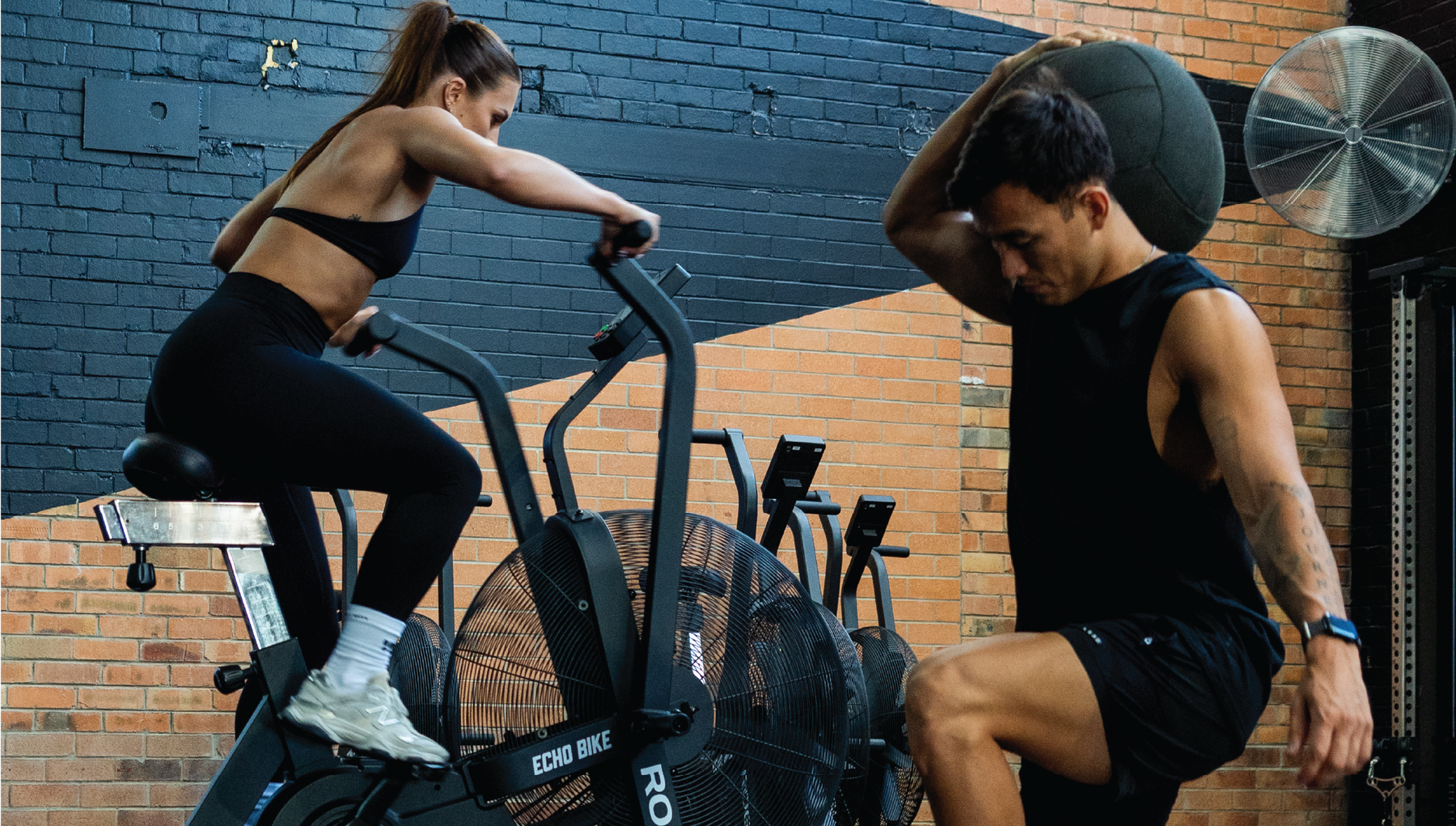 Two people exercising in a gym, one on an exercise bike and one lifting.